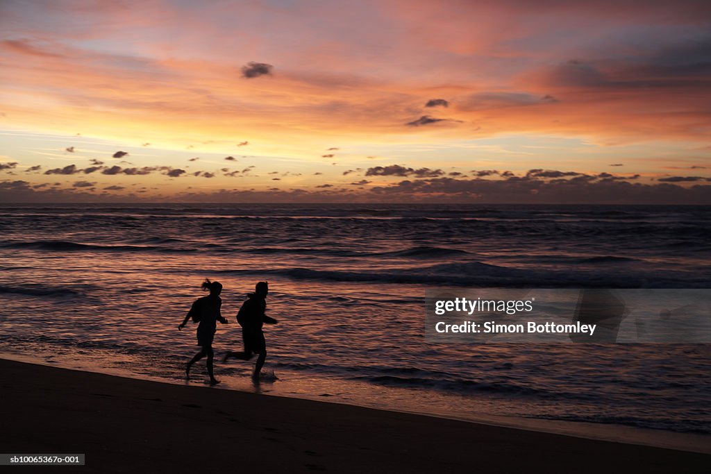 Silhouettes of two joggers on beach at sunset