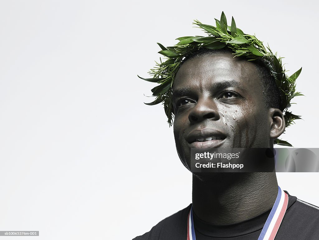 Man crying with crown of leaves on head, wearing medal, close-up