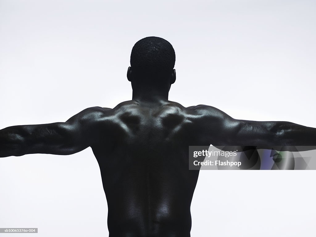 Muscular man standing with arms out, rear view, close-up