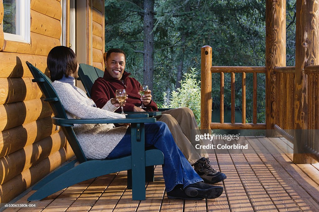 Couple on porch sitting in Adirondack chairs, drinking wine