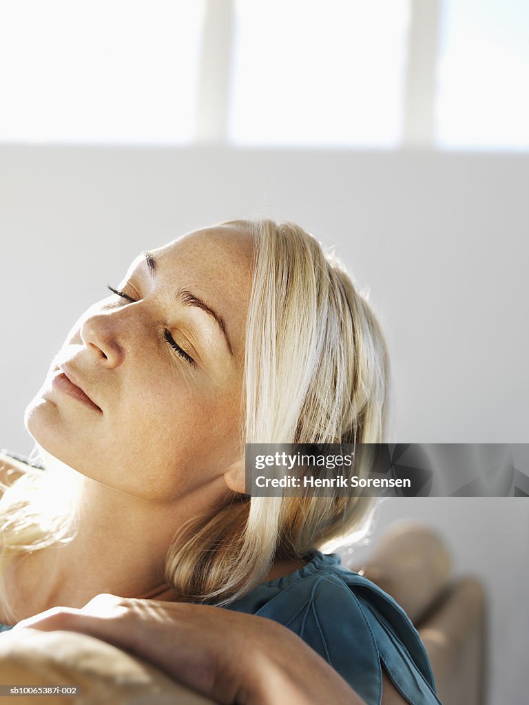 Close-up of mid adult woman sitting on sofa, eyes closed