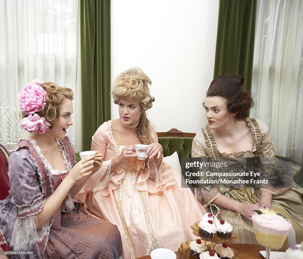 Three young women in period dress talking at tea party