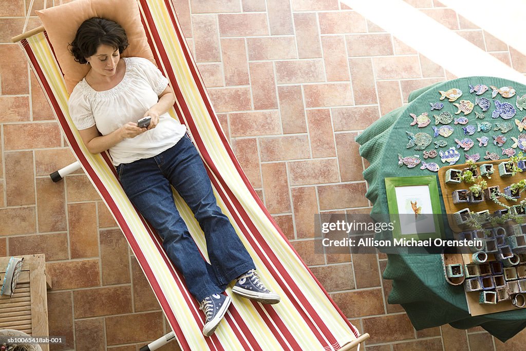 Woman texting on cell phone on hammock in house, elevated view