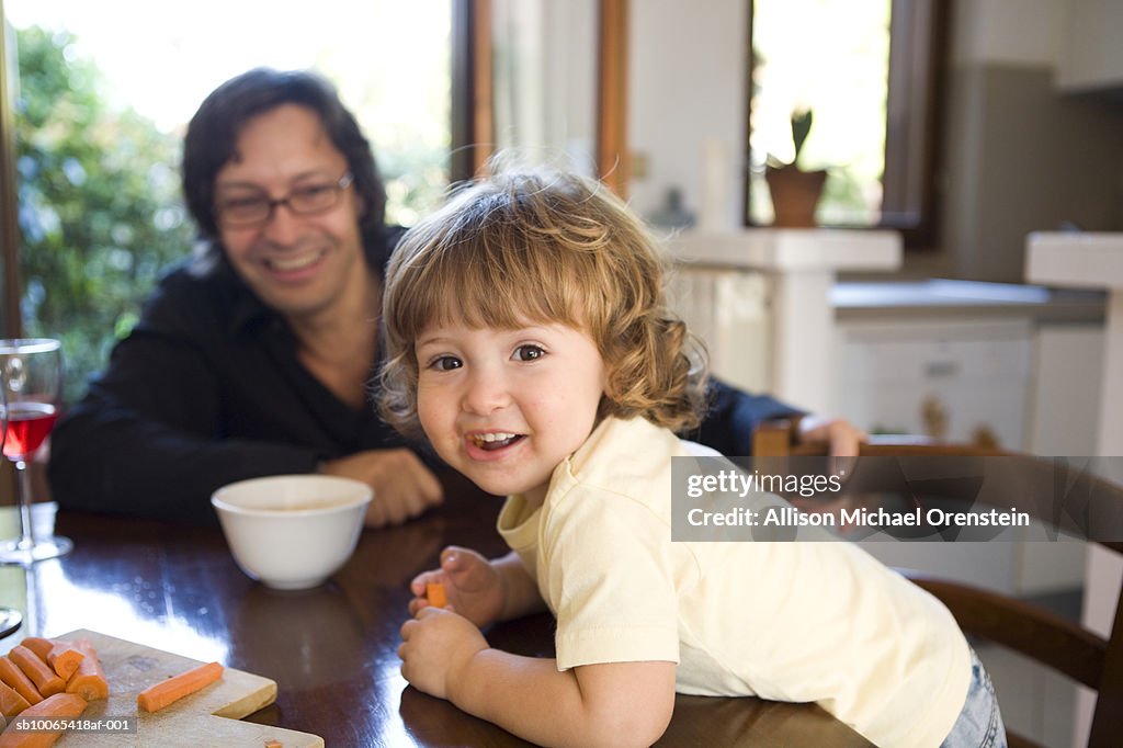 Father and daughter (2-3) in dining room eating carrots