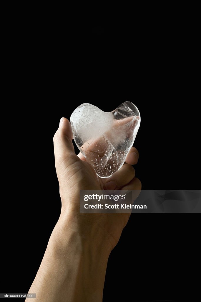 Man holding heart made of ice, black background