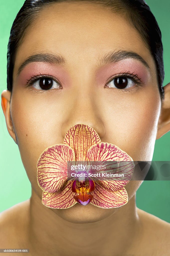 Portrait of  young woman with orchid flower in mouth