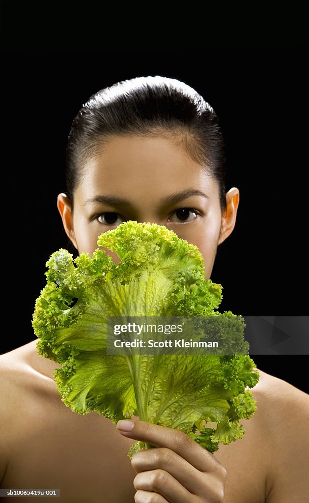 Portrait of young woman with kale leaf, black background