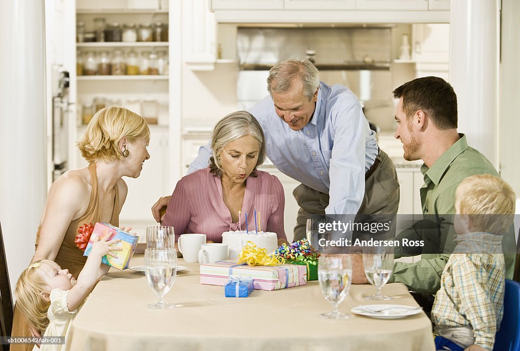 Family with baby daughter (9-12 months) and son watch as grandmother blows out candles on Birthday Cake