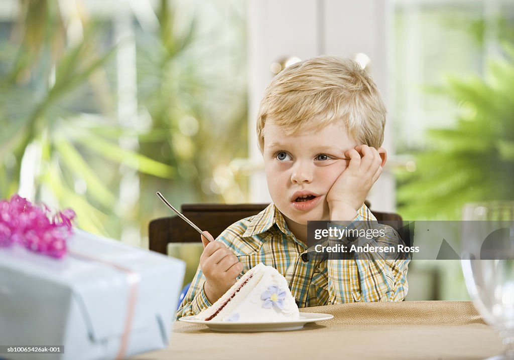 Boy (2-3 years) bored in front of cake and gifts