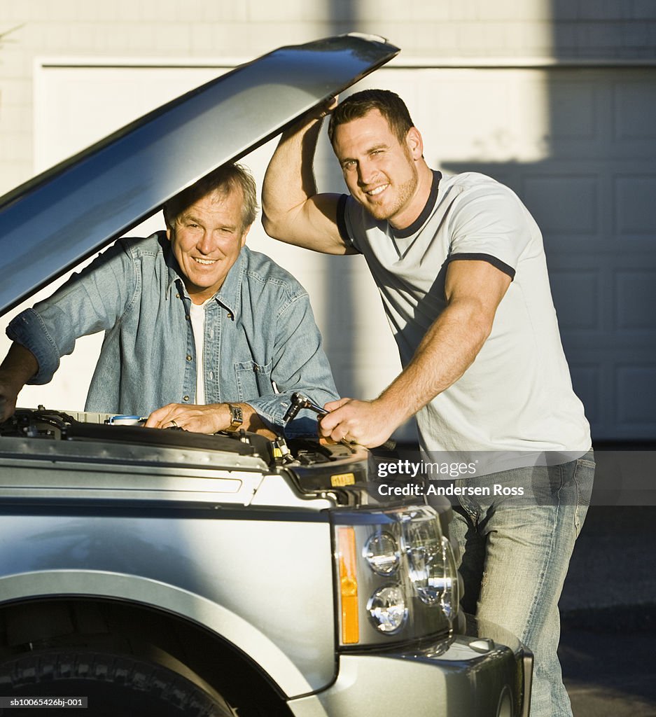 Portrait of two men examining engine of car