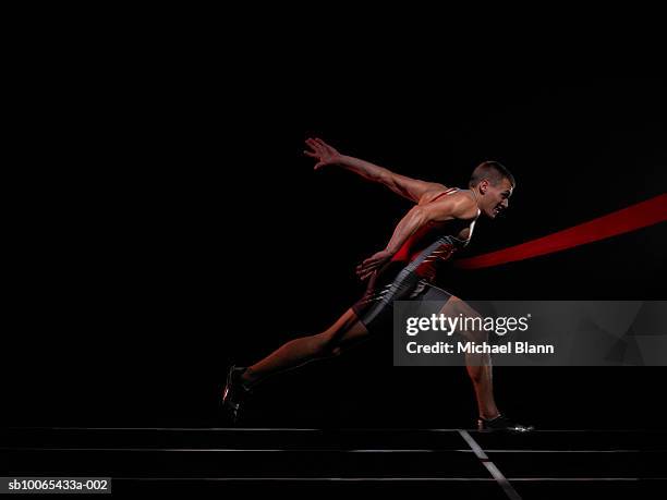 sprinter running through finish line, studio shot, side view - finishing line stock pictures, royalty-free photos & images