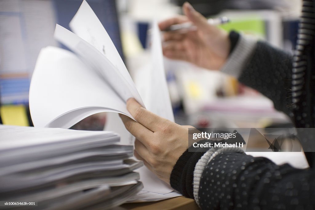 Office worker checking documents on desk, mid section, side view