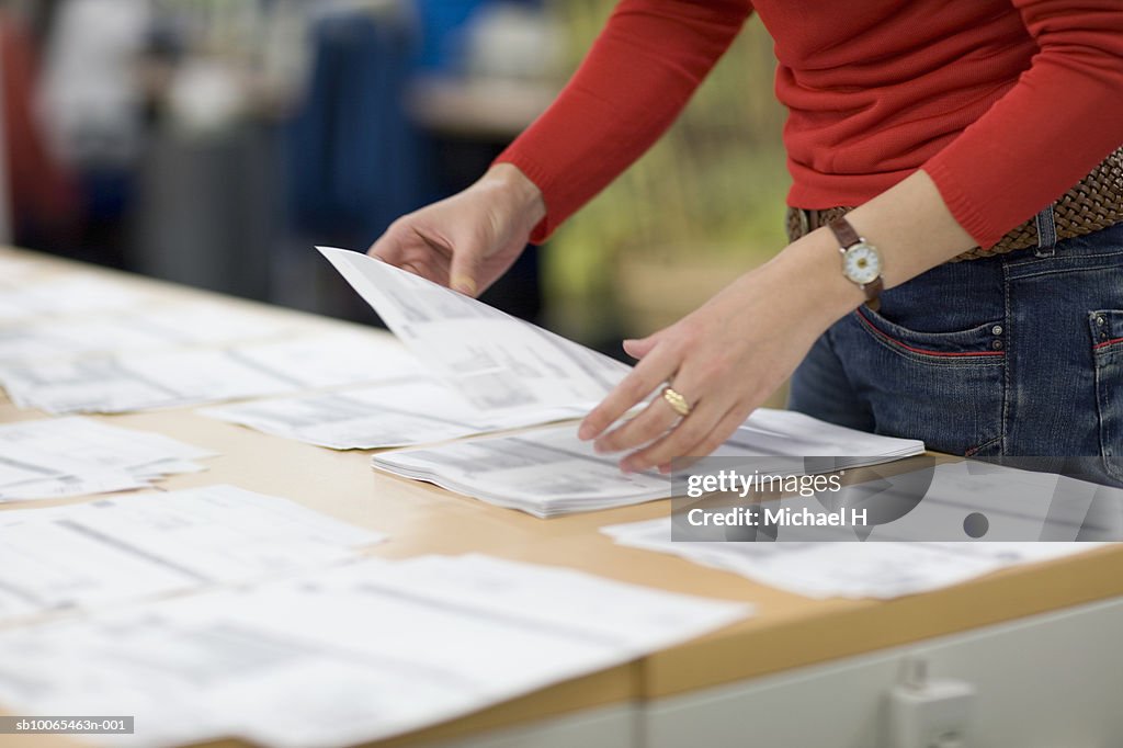 Female office worker arranging document on desk, mid section