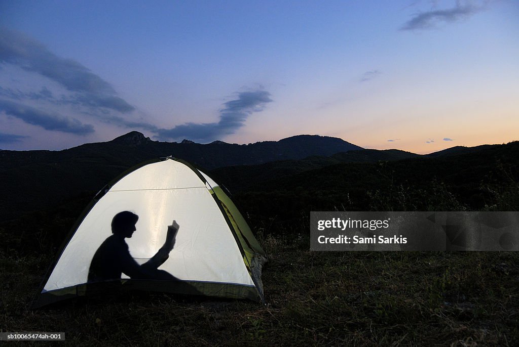 Silhouette of woman in illuminated tent, reading book