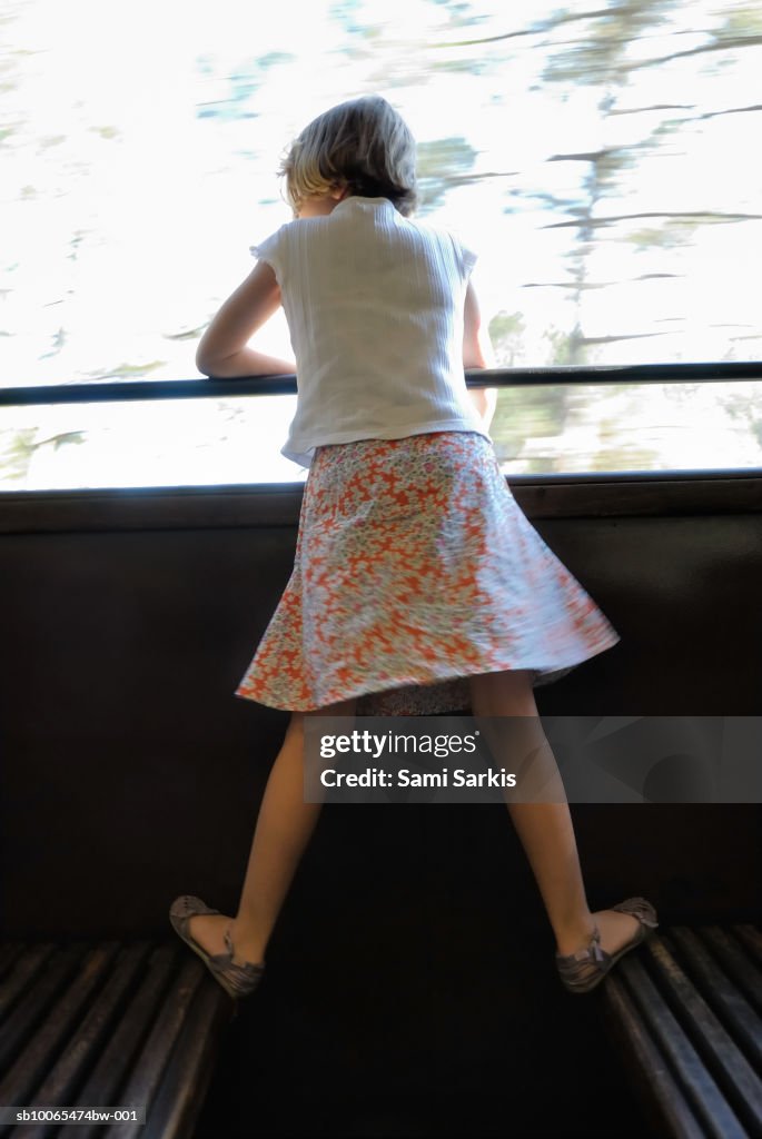 Girl (6-7) looking out window of speeding train, rear view