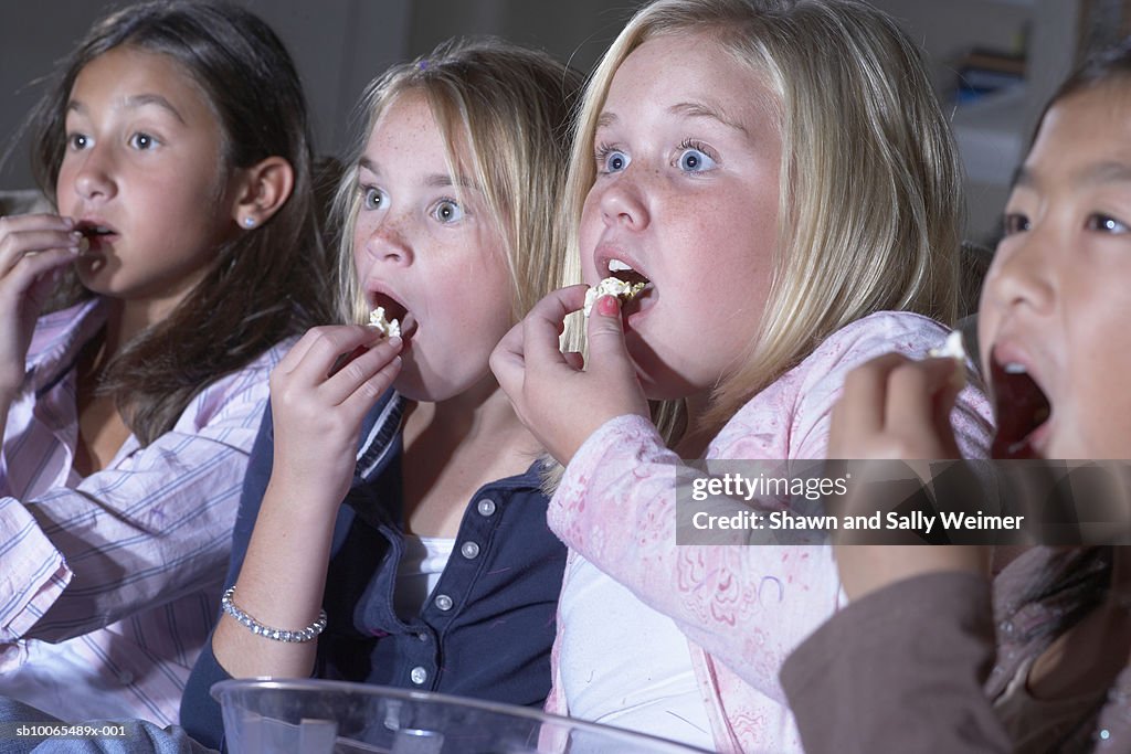 Four girls (10-11 years) eating popcorn watching television with frightened expressions