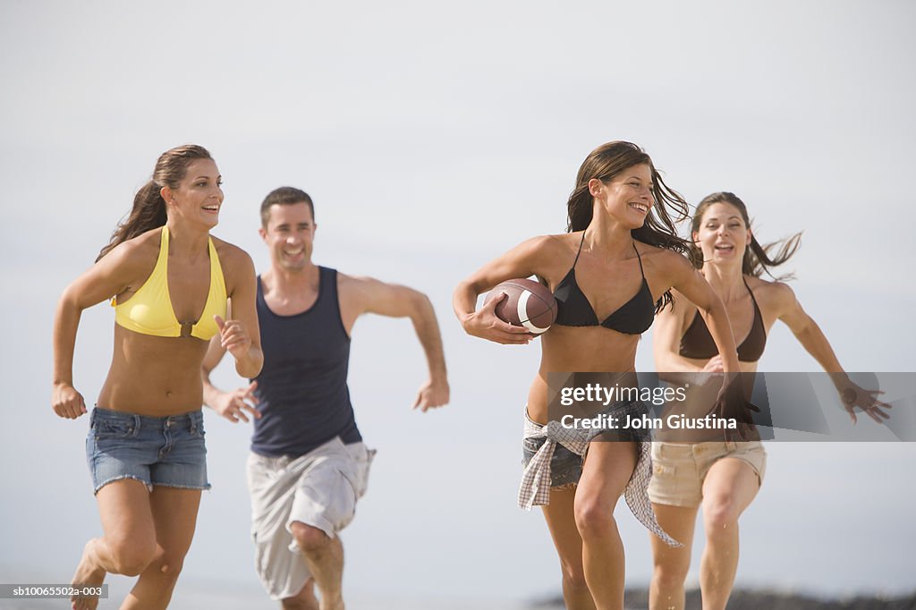 Young women and man playing American football on beach