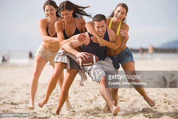 young women tackling man playing american football on beach - man met een groep vrouwen stockfoto's en -beelden