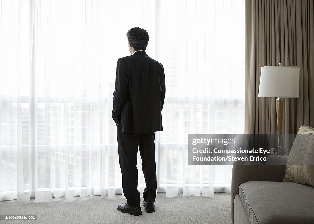 Businessman in hotel room, looking out window, rear view