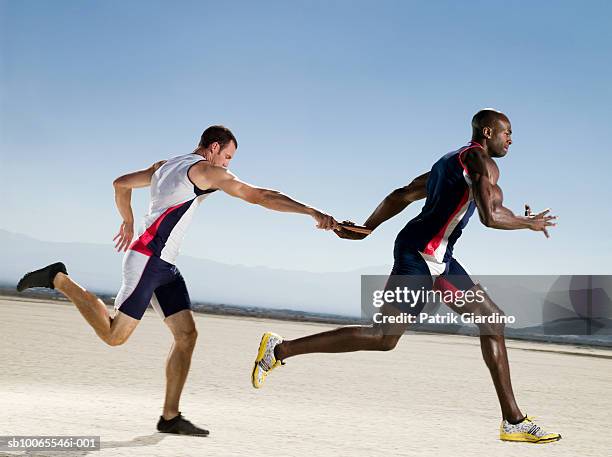 two athletes passing relay, side view - relay fotografías e imágenes de stock