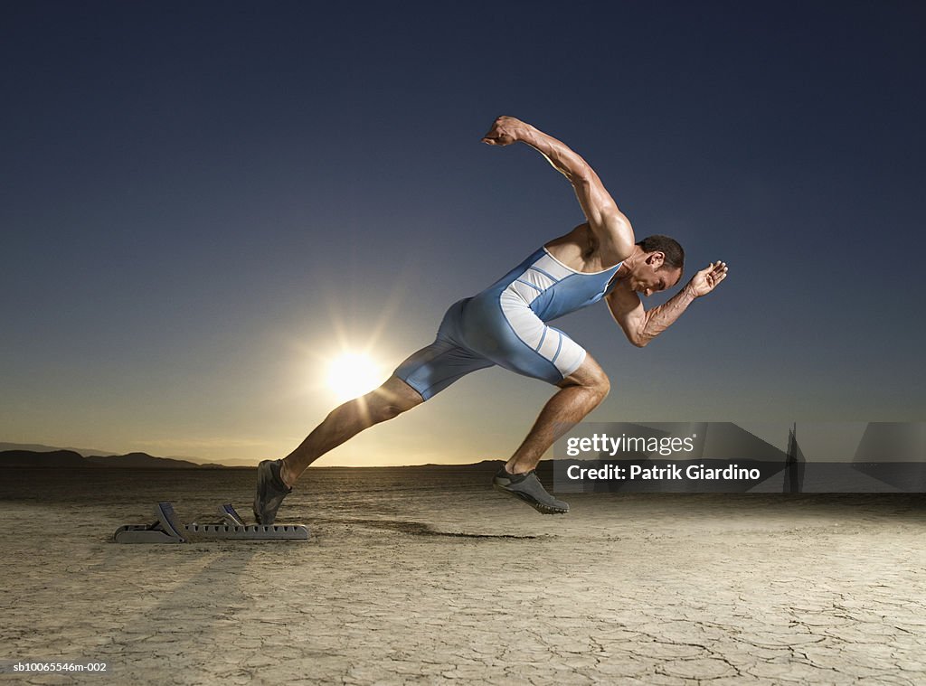 Athlete running from starting block at dusk, side view