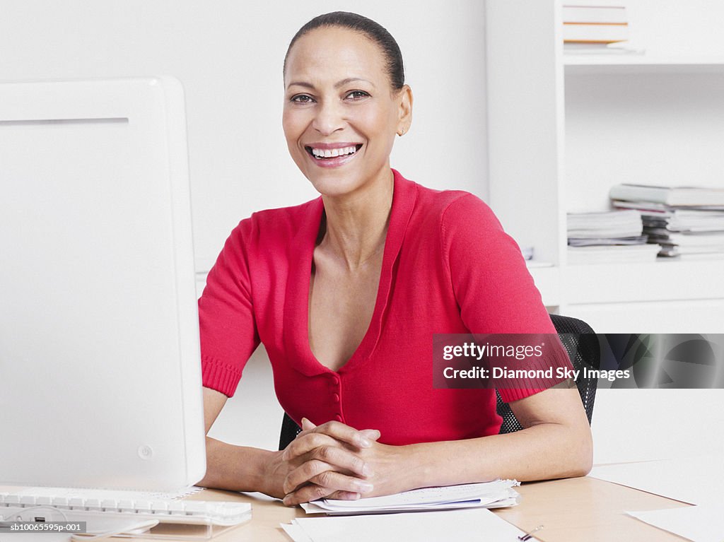 Business woman sitting behind desk, smiling, portrait