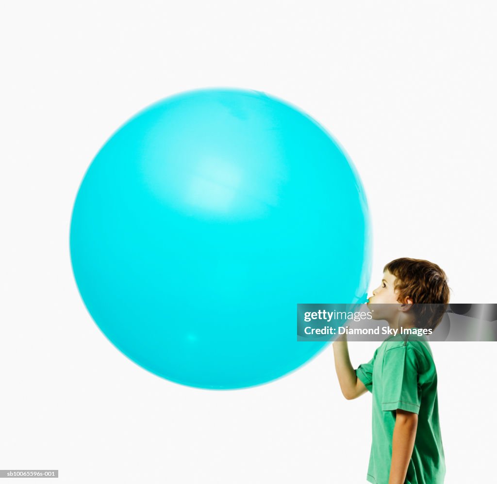 Boy (6-7) blowing balloon, side view