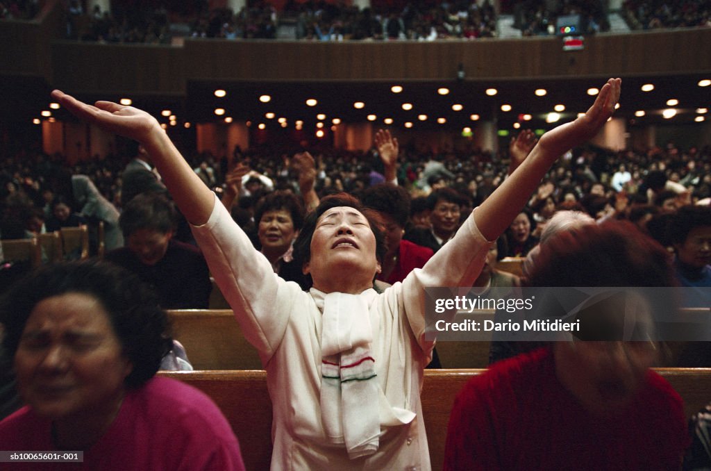 People praying, one woman standing with raised arms