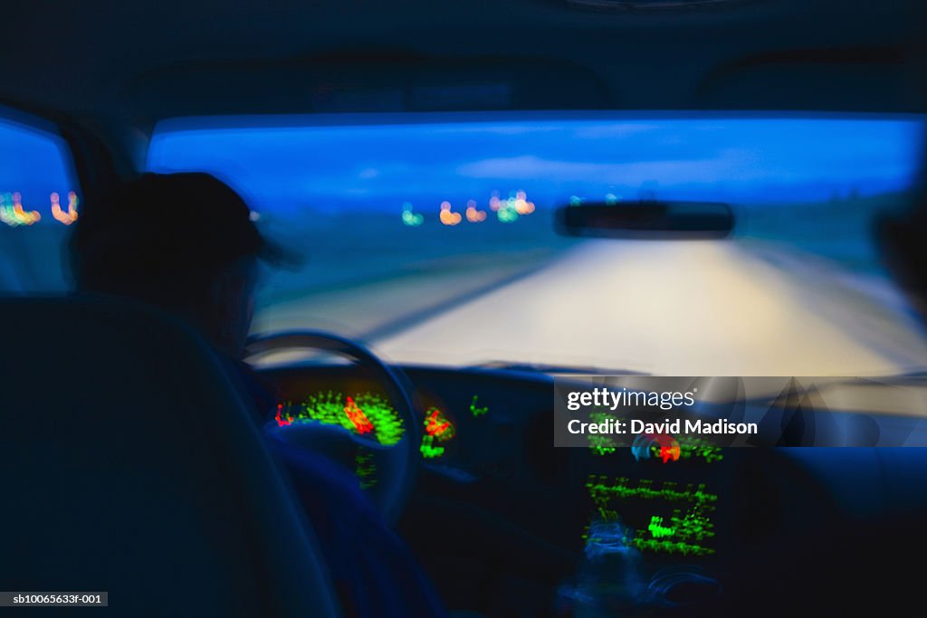 Mature man driving car at dusk, blurred motion, rear view