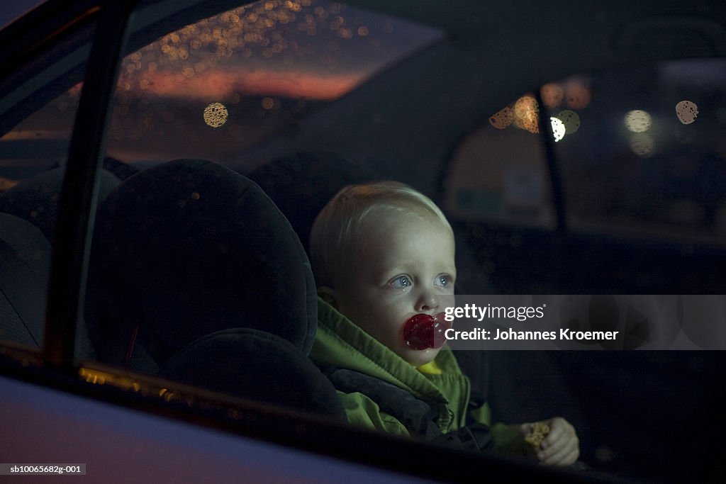 Baby boy (12-18 months) sitting in back seat of car, night