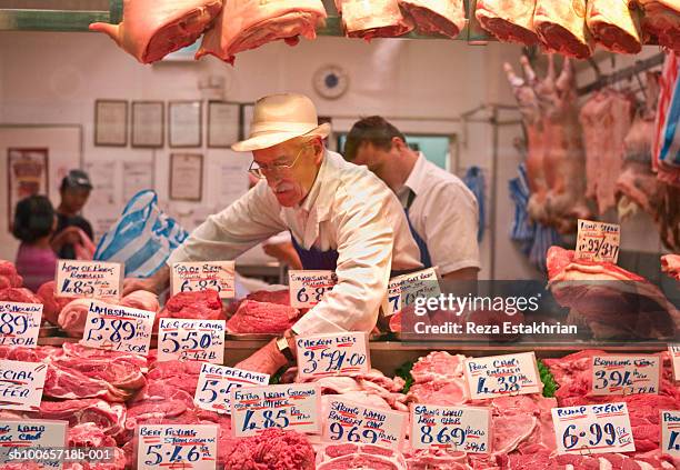 butcher arranging meat at store window - butcher foto e immagini stock
