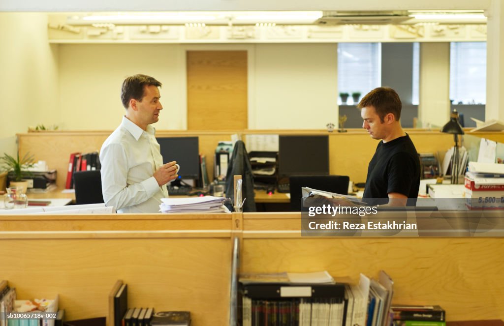Two businessmen having coffee break while chatting across office divider