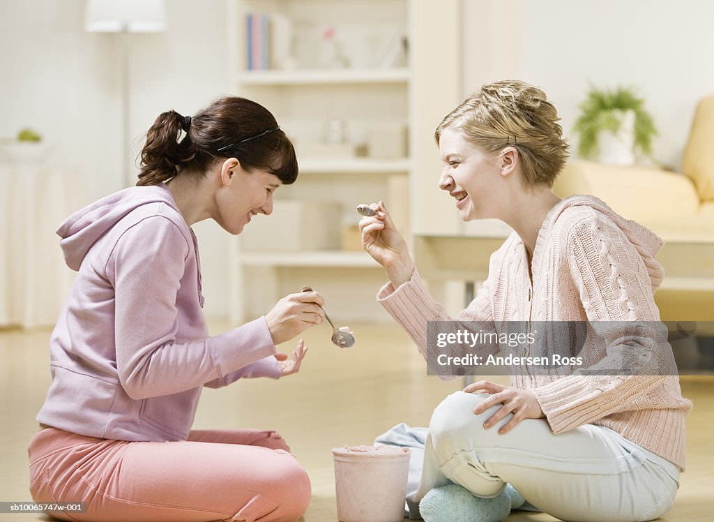 Two young women sitting on floor eating ice cream, side view