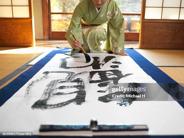japan, tokyo,woman wearing kimono writing calligraphy on large piece of paper - japanese brush stroke stock pictures, royalty-free photos & images