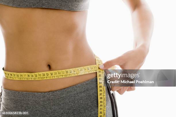 woman measuring waist using tape measure, mid section - waist stockfoto's en -beelden