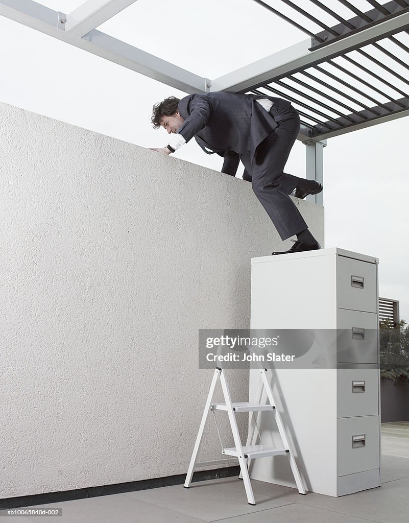 Mature businessman climbing on wall through filing cabinet in office