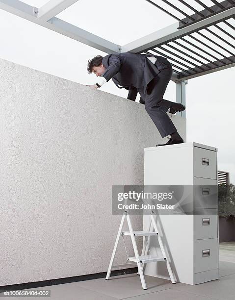 mature businessman climbing on wall through filing cabinet in office - escaping office stock pictures, royalty-free photos & images