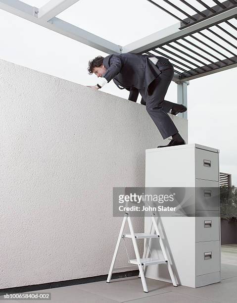 mature businessman climbing on wall through filing cabinet in office - escapismo - fotografias e filmes do acervo