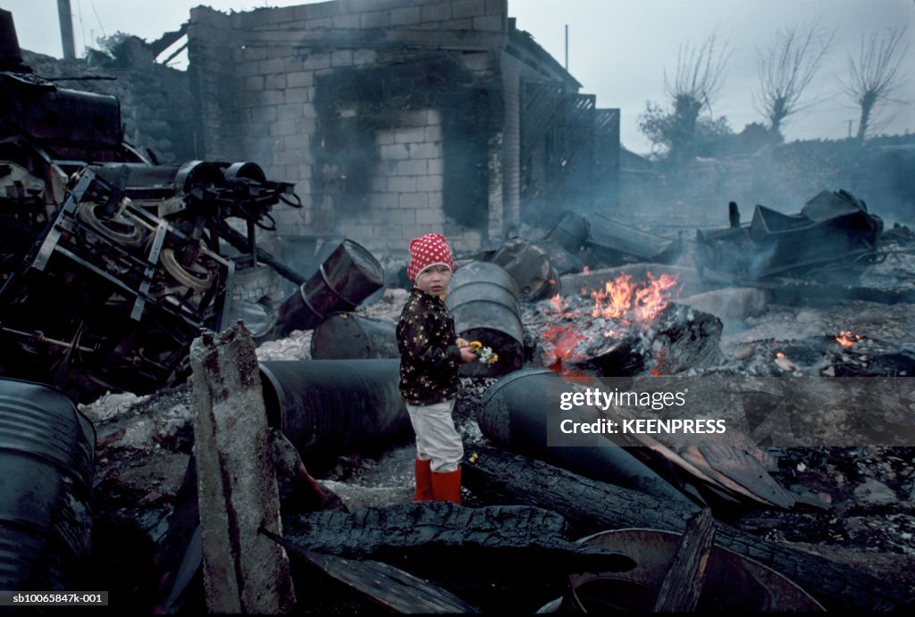 Estonia, girl standing in charred rubble and oil drums left over from Soviet occupation in small village