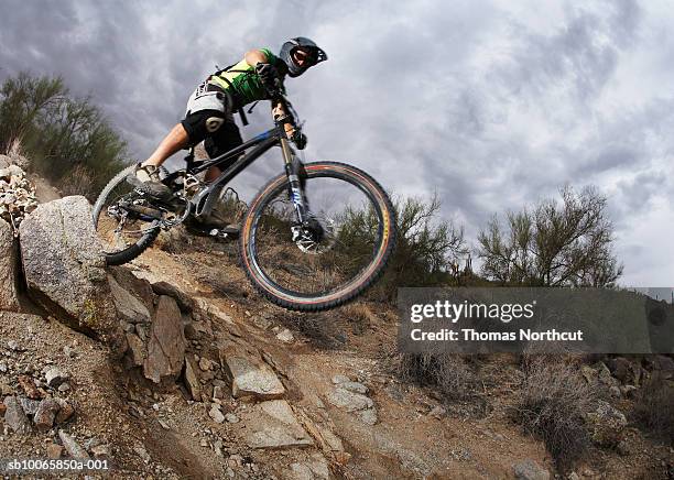 man mountain biking down steep rocky path, low angle view - andare in mountain bike foto e immagini stock