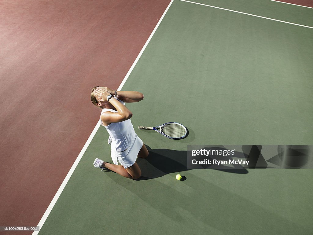 Young woman kneeling on tennis court, hand in hands
