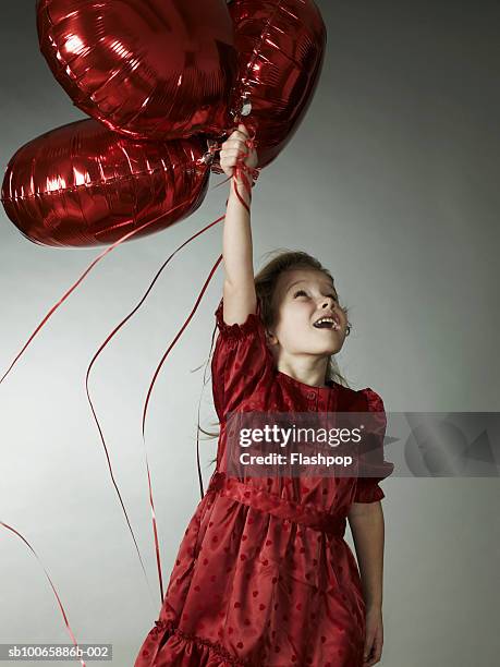girl (6-7) holding heart shaped balloons, smiling - child balloon studio photos et images de collection
