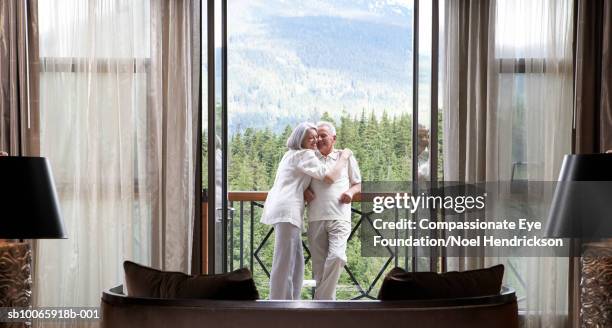 mature couple standing on balcony, hugging - matching outfits stock-fotos und bilder