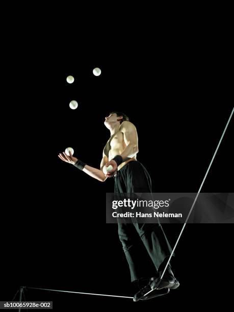 male gymnast standing on tightrope, juggling balls, low angle view - malabarismo imagens e fotografias de stock