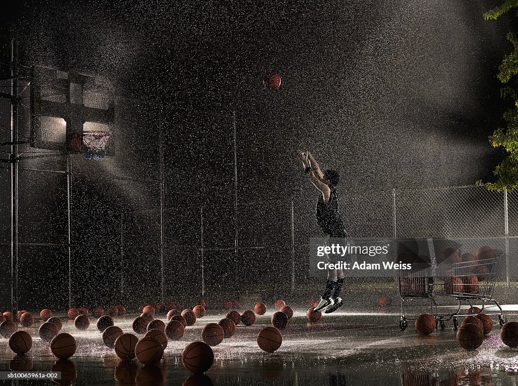 Man shooting basketball at night in rain, side view