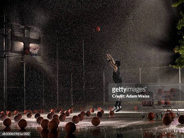 man shooting basketball at night in rain, side view - determination stock-fotos und bilder