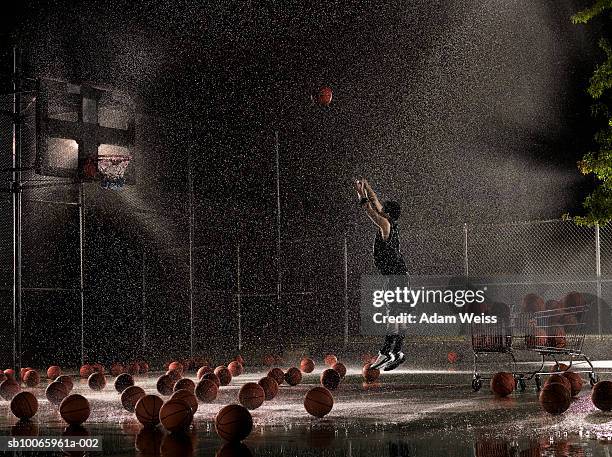 man shooting basketball at night in rain, side view - basketball sport - fotografias e filmes do acervo