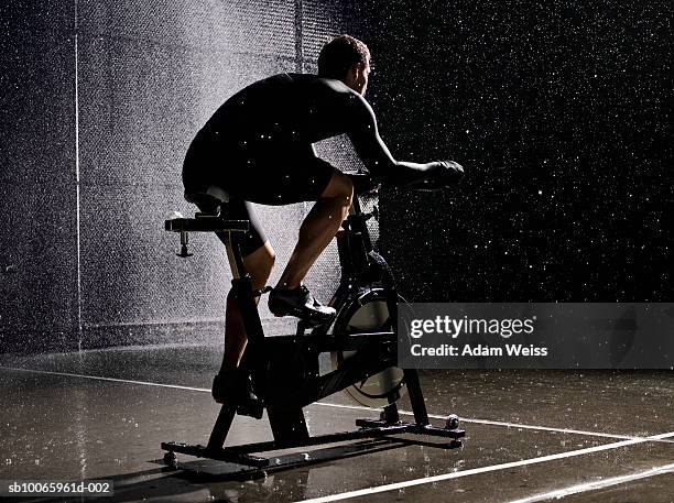 man using exercise bike in basketball court at night - heimtrainer stock-fotos und bilder