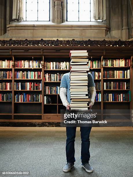 young man carrying stack of books in university library - bookshelf photos et images de collection