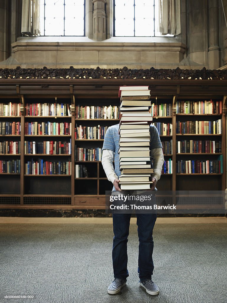 Young man carrying stack of books in university library